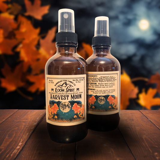 Two bottles of 'Harvest Moon' room spray on a wooden surface with autumn leaves in the background.